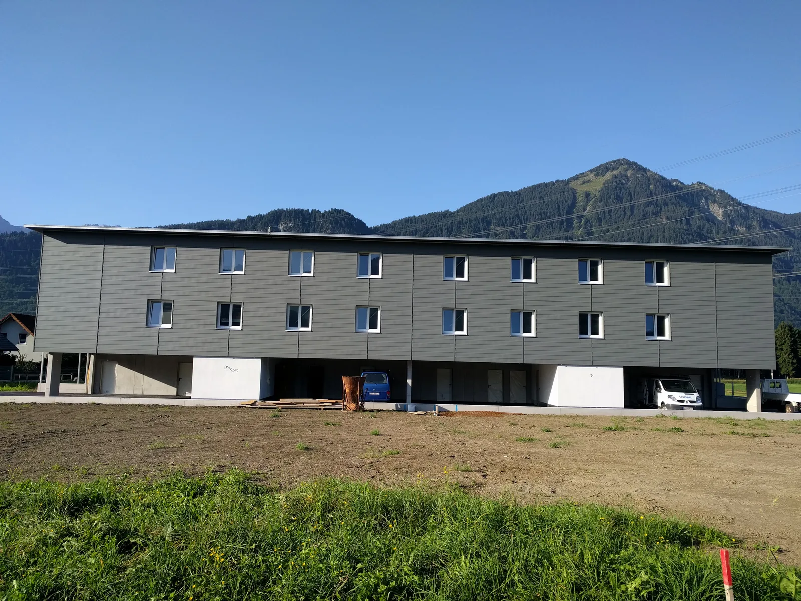 Fertige dreigeschossige Wohnanlage mit dunkler Fassade und Balkonen, davor eine Wiese