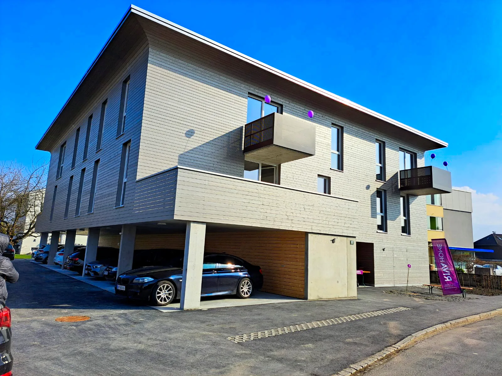 Fertiges Wohnhaus mit heller Holzfassade, Balkonen und offenem Carport im Erdgeschoss