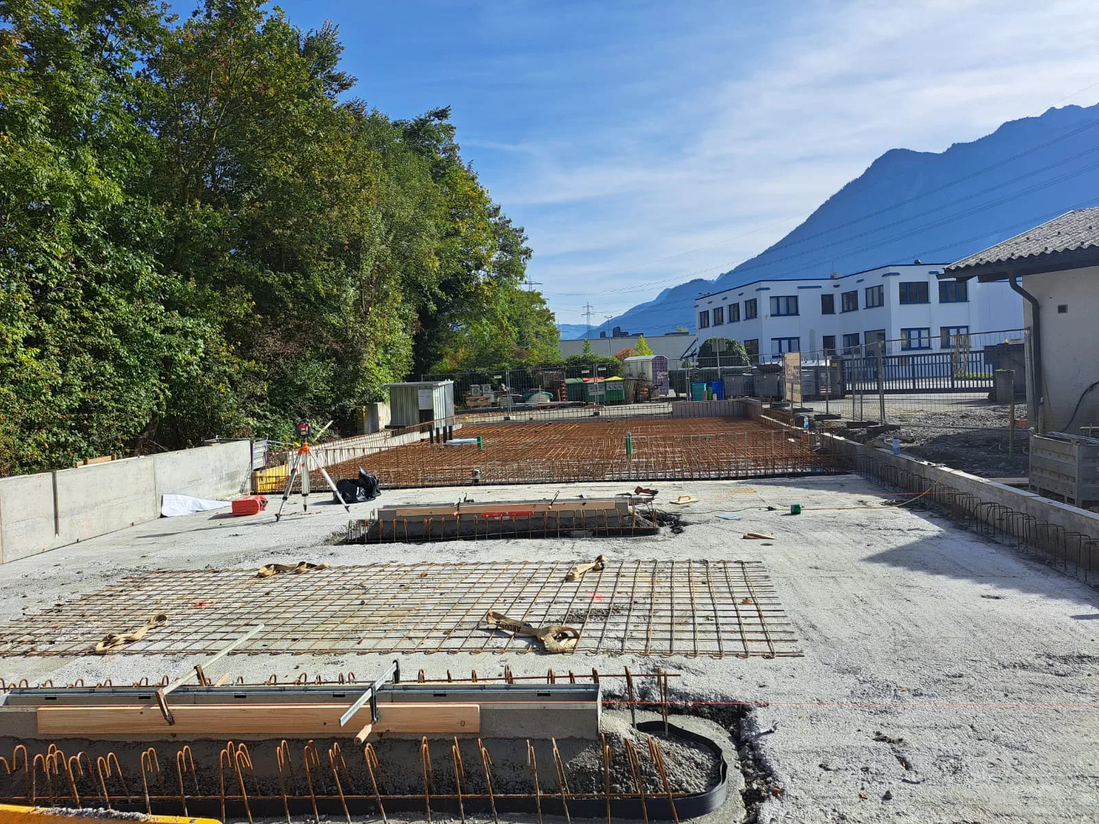 Großflächige Bewehrung vor einer Betonmauer, im Hintergrund Berge und blauer Himmel